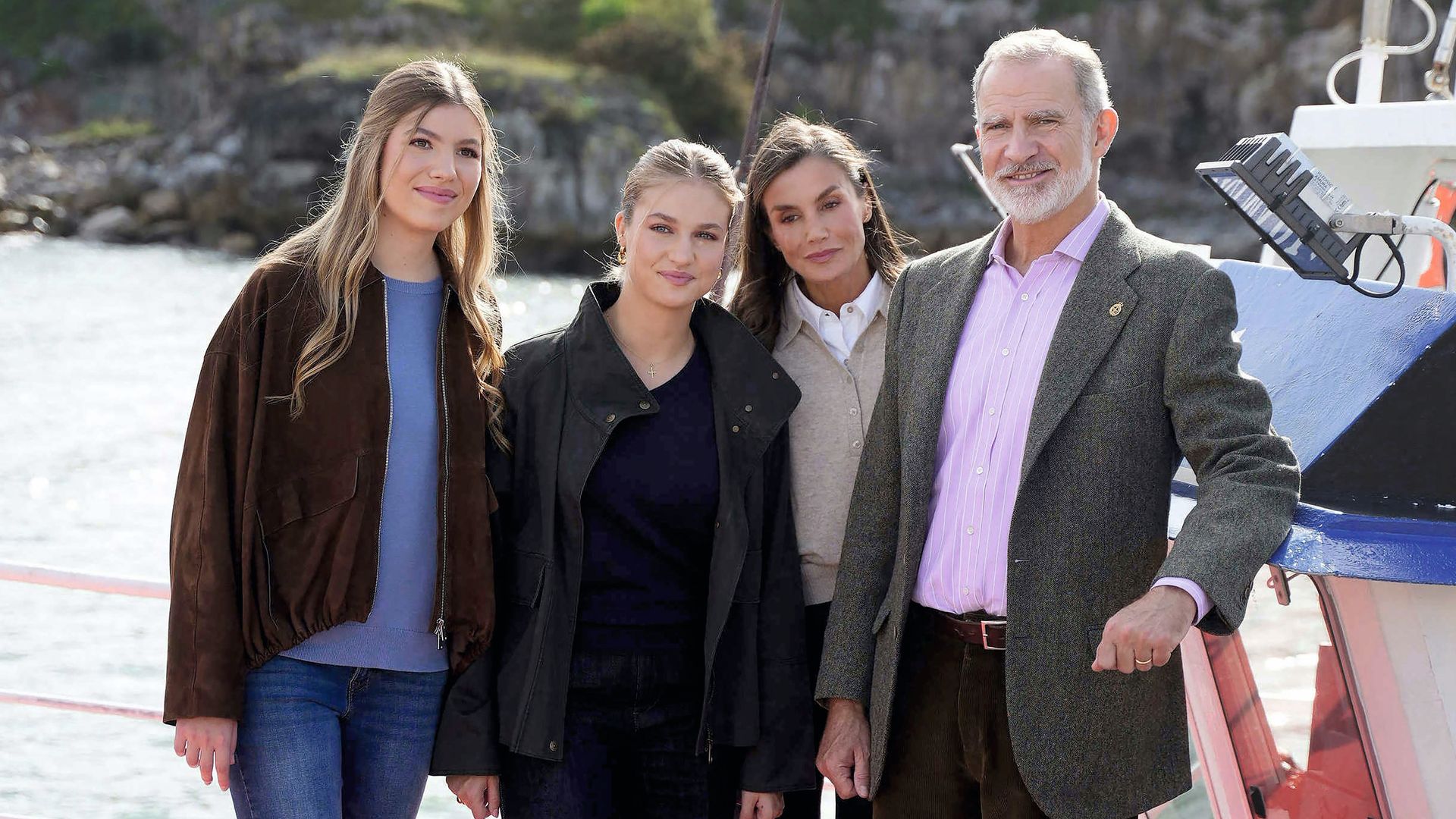 La infanta Sofía (con 'bomber' de ante, de Massimo Dutti, y jersey de punto fino azul), la princesa Leonor (con parka encerada de Mango, jersey azul marino y vaqueros anchos) y los Reyes Felipe y Letizia en el puerto de Llanes