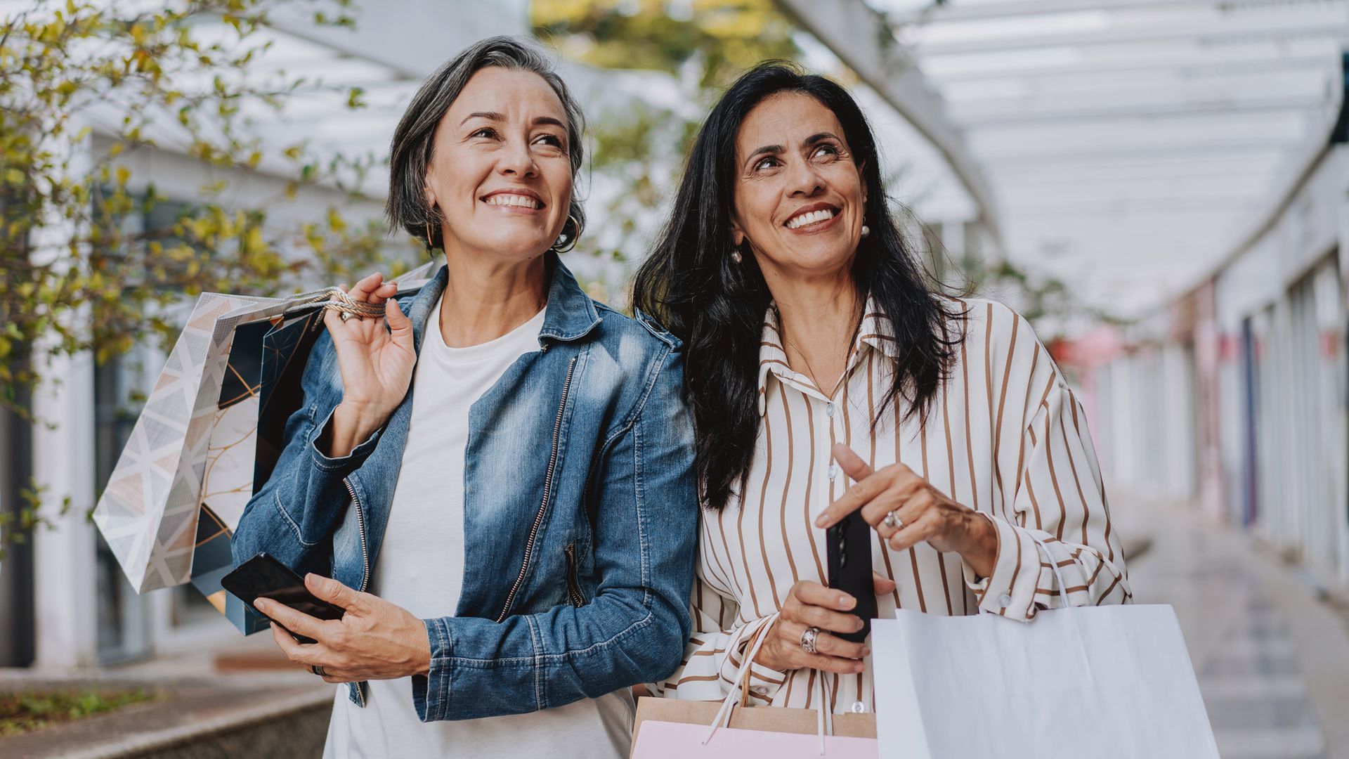 Dos mujeres de más de 50 años (silver) sonriendo y comprnado en un centro comercial en otoño-invierno.