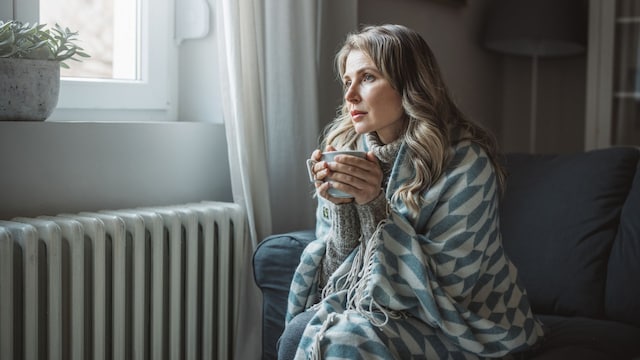 mujer con frío en casa, con una manta y una taza de café