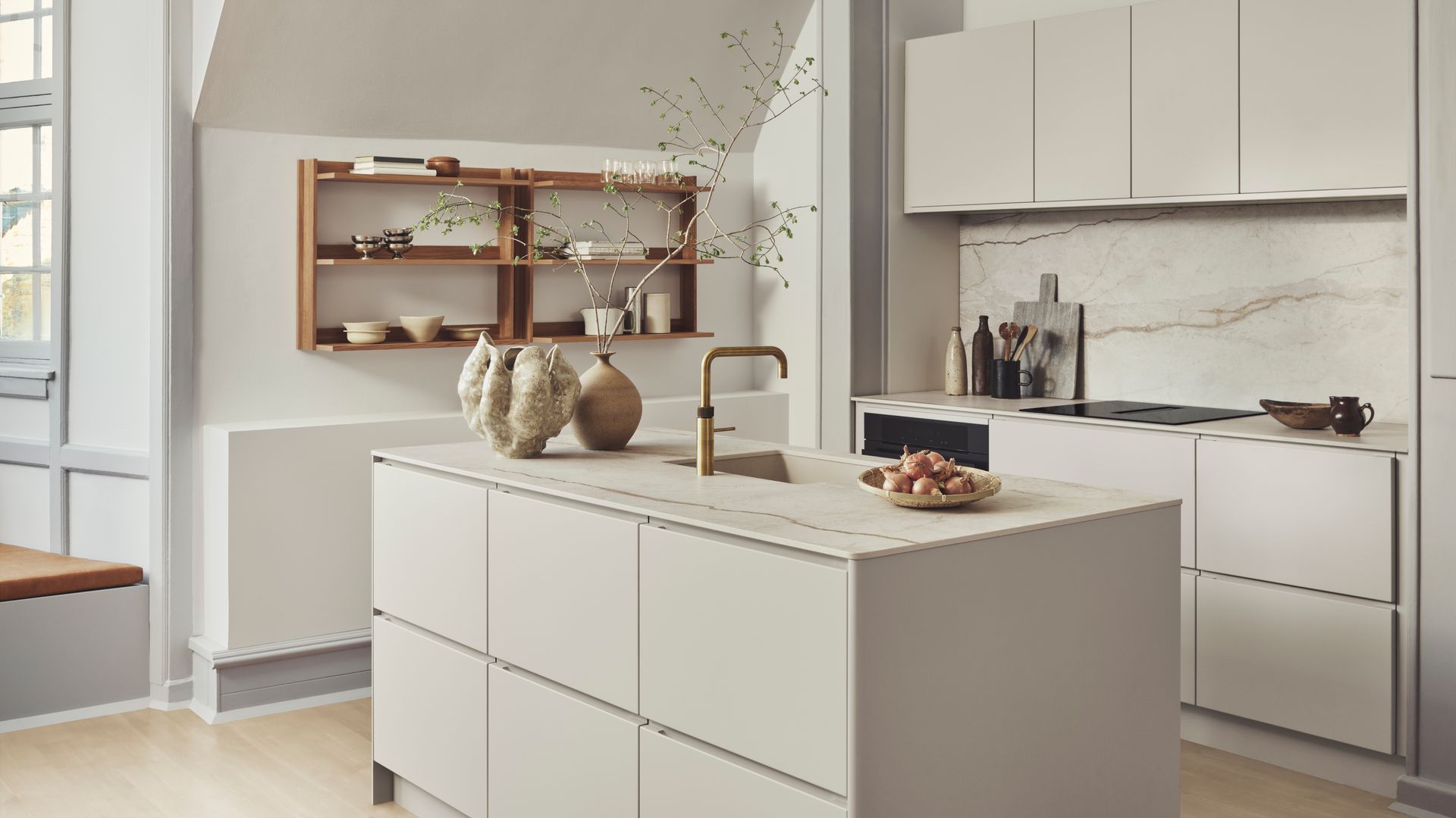 Cocina con isla en color crema, con estantería de madera y muebles altos