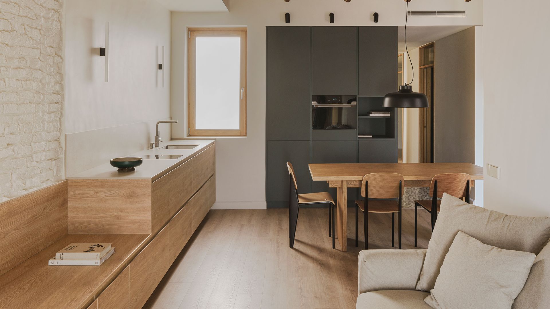 Cocina abierta con banco de madera, bóveda catalanas, suelo de madera, ventana de madera, campana en el techo, sofá beige