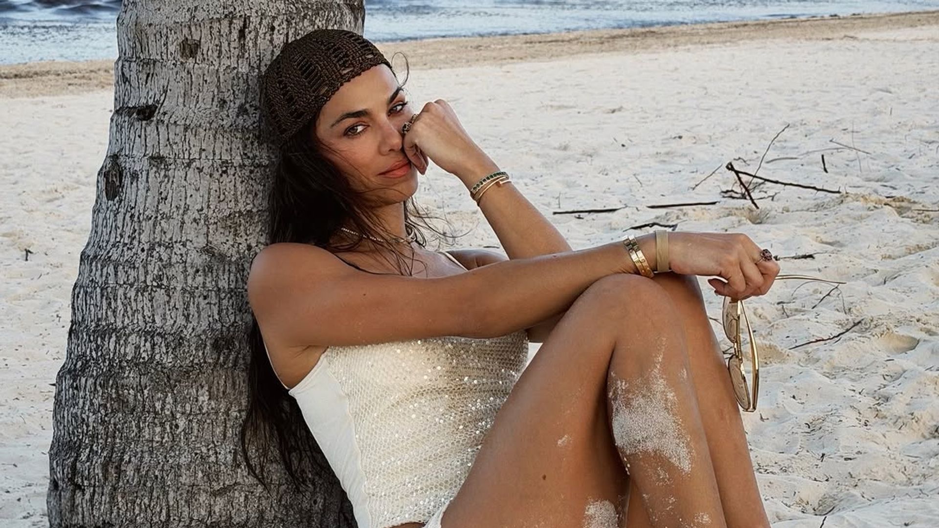 Una chica apoyada en una palmera en la playa con look veraniego