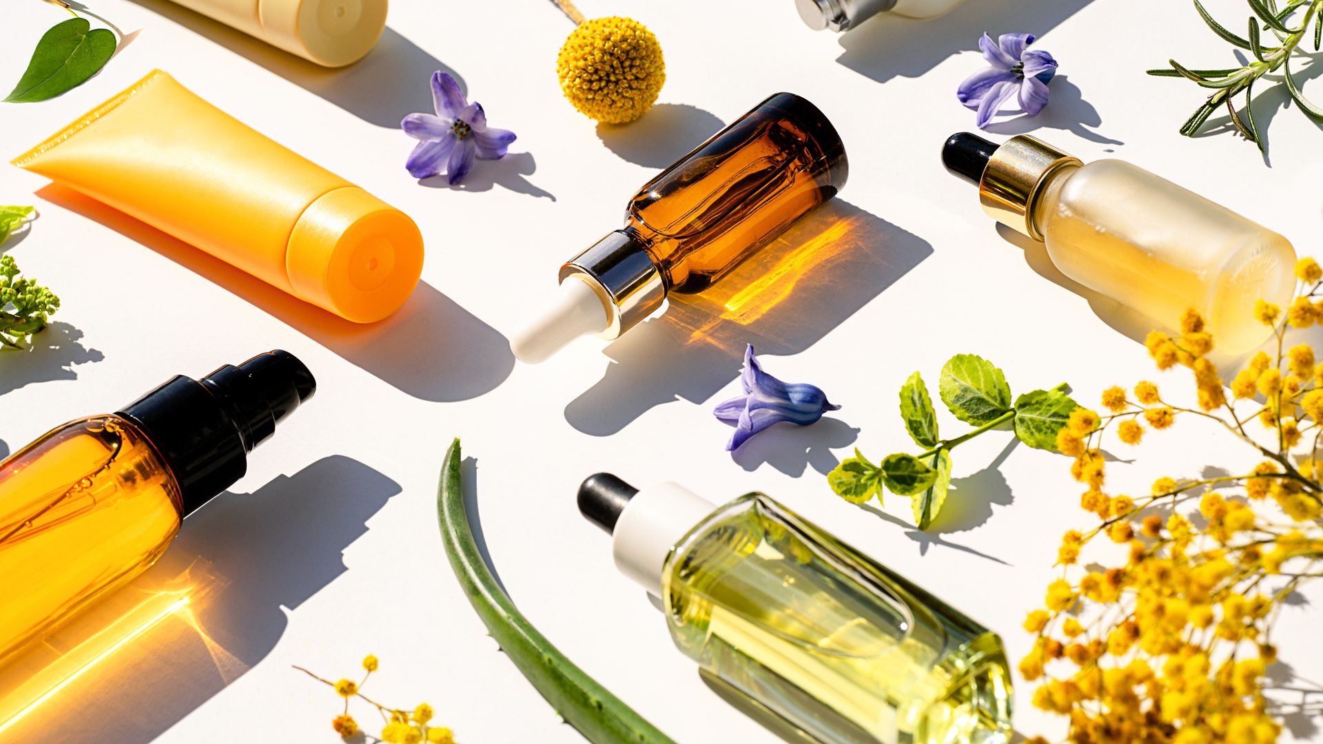 Bodegón de cremas y sérums sobre fondo con plantas y flores