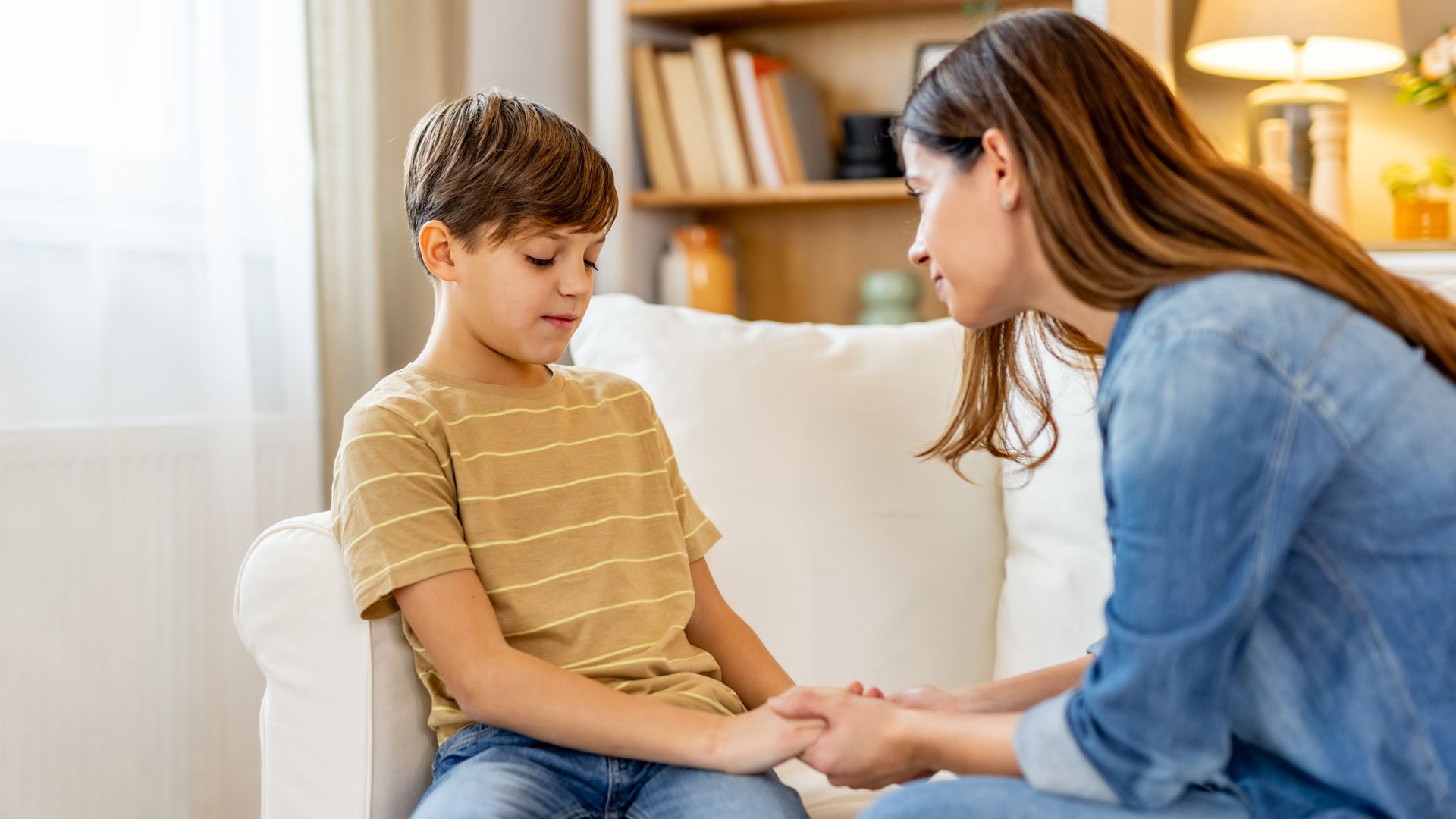 madre hablando con su hijo, al que le da la mano, sentados en el sofá