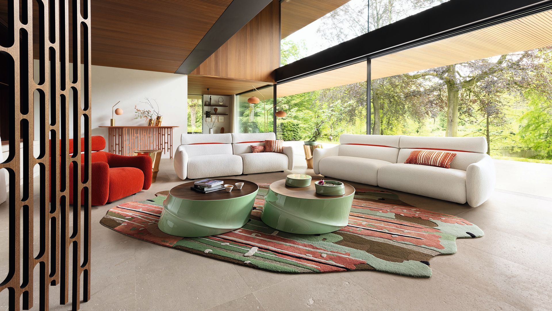 Salón con grandes ventanales con vistas al jardín, sofá blanco, mesas de centro verdes, alfombra en verde, marrones y rojos, sillón rojo 