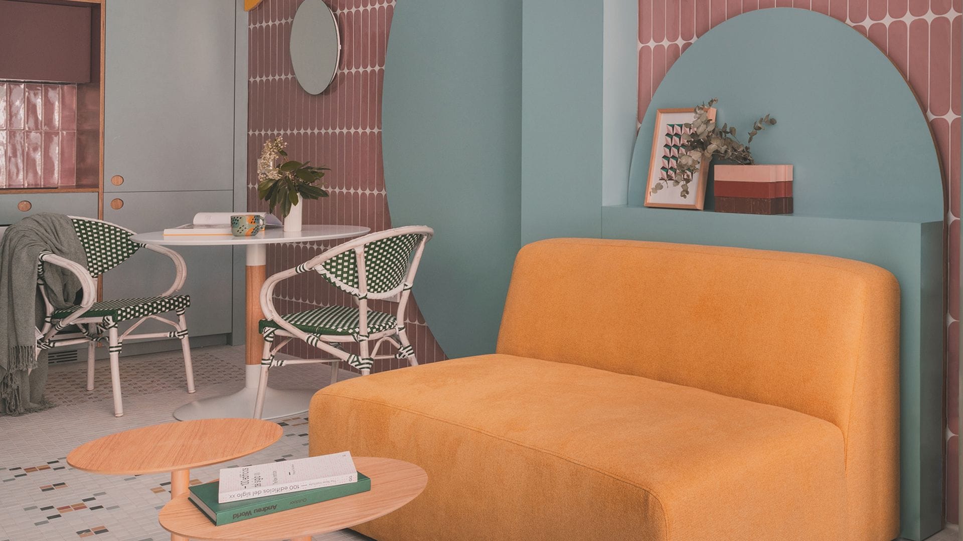 Salón comedor con sofá amarillo, paredes de azulejos rosas, suelo de baldosas, estructura de madera circular en azul claro