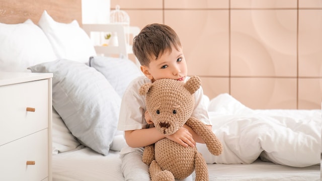 Niño sin poder dormir abrazado a su oso sentado en la cama