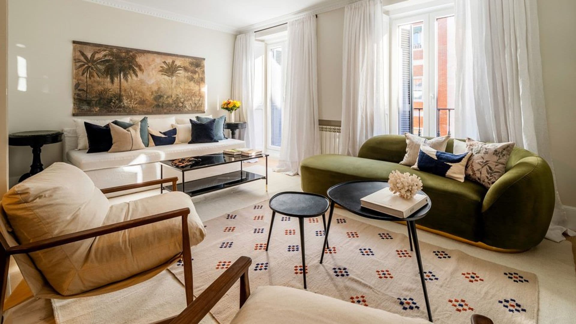 Salón con sofá blanco, sofá verde de terciopelo y formas curvas, alfombras, cortinas blancas, butaca, mural en la pared del sofá, mesas auxiliares negras