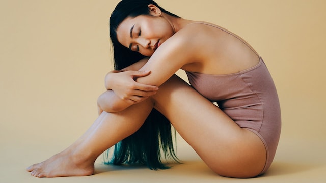 Mujer asiática con body sentada abrazada a sus rodillas