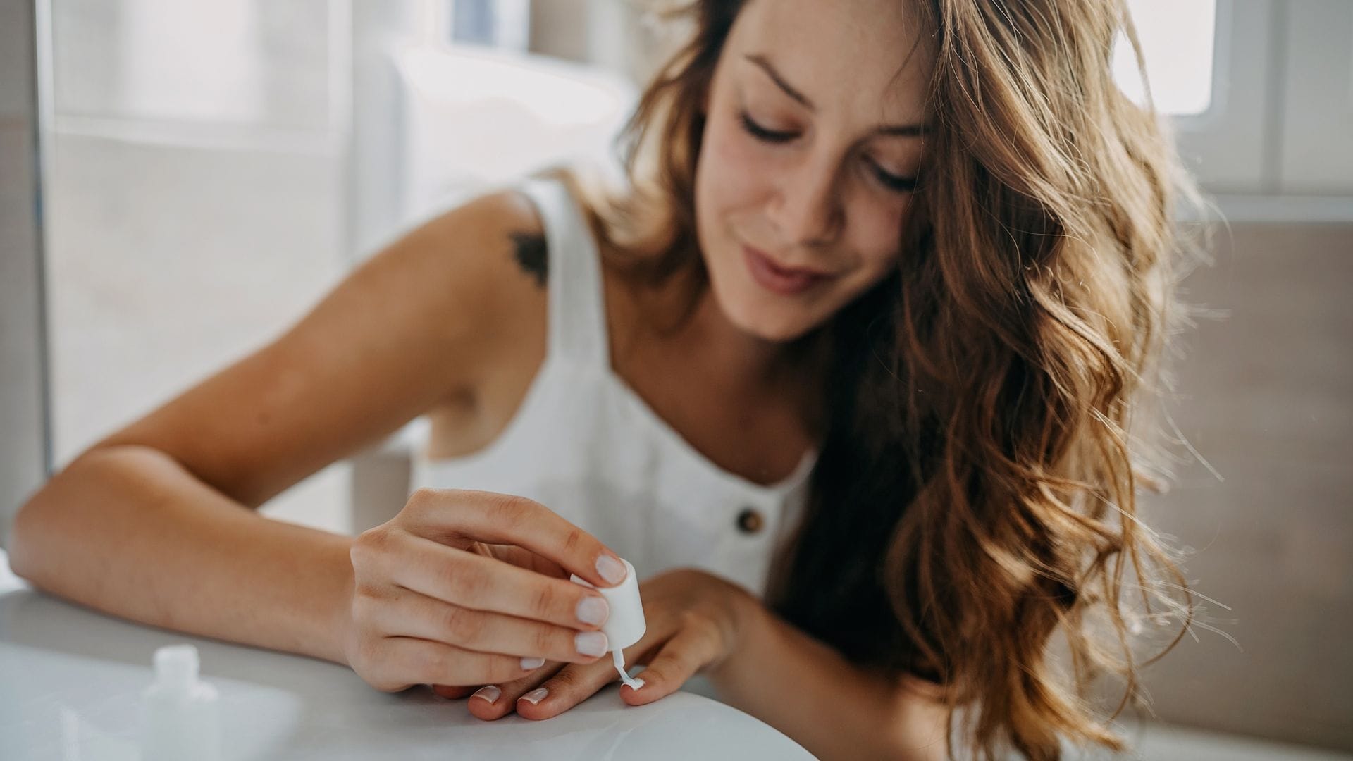 Mujer joven pintándose las uñas en el cuarto de baño