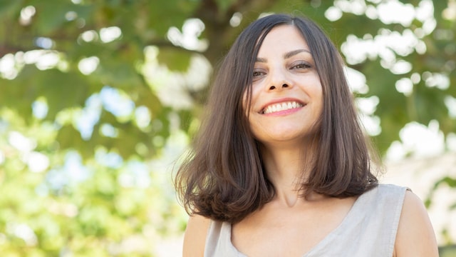 Mujer de 40 años sonriendo a la cámara en el exterior con un fondo verde de árboles.