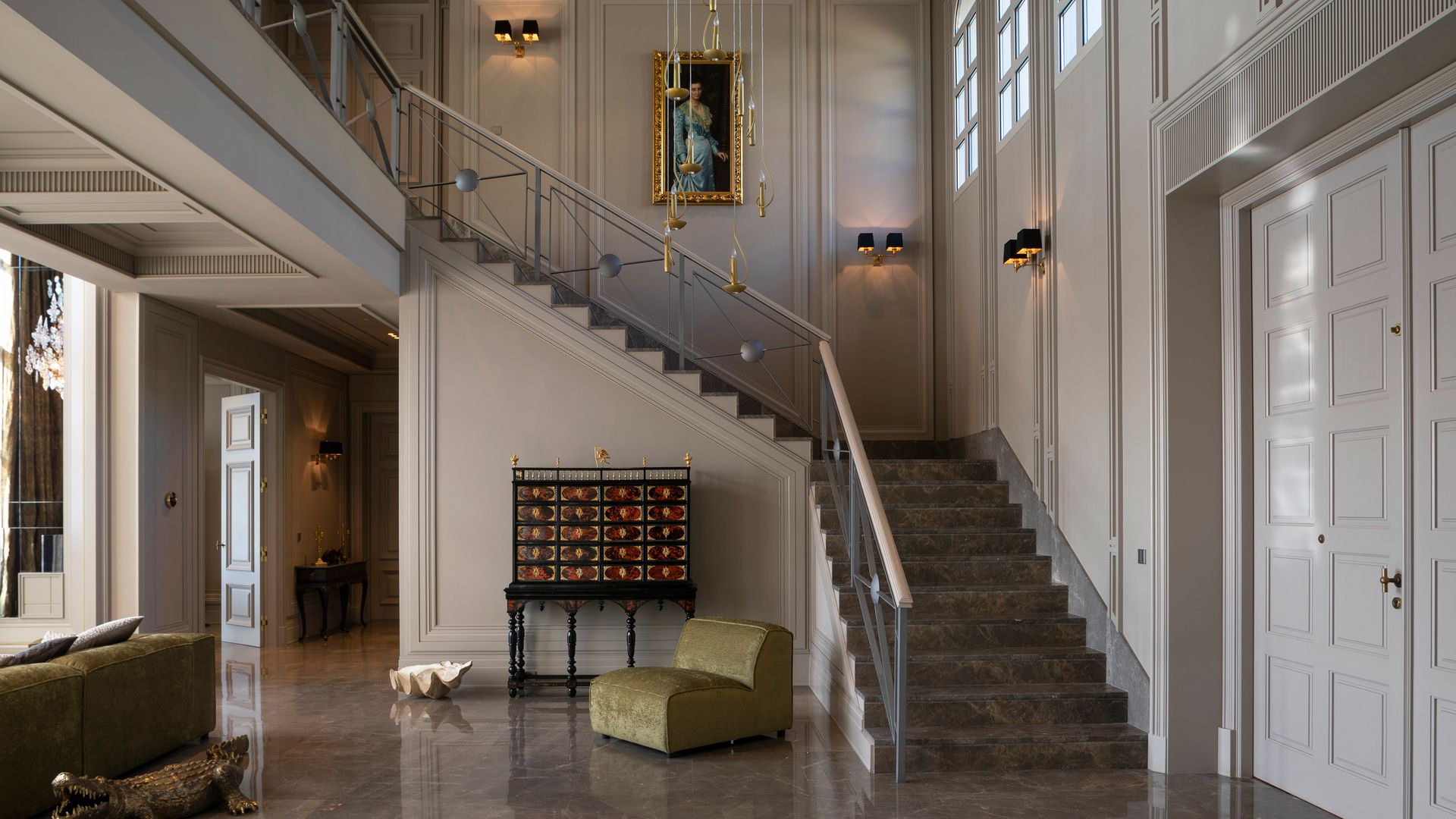 Recibidor espectacular con subida de escalera y suelo de mármol, molduras en las paredes, mueble de estilo chino, butaca verde, cuadro en la subida de la escalera