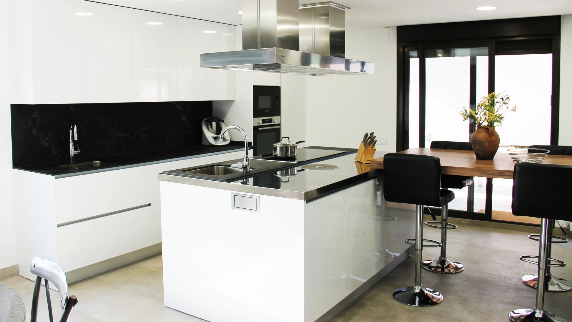 Cocina en blanco y negro, con isla y mesa adosada con taburetes, campanas de techo