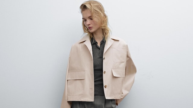 Mujer rubia mirando al suelo con pantalones de pinzas, polo de punto y cazadora corta beis de Massimo Dutti