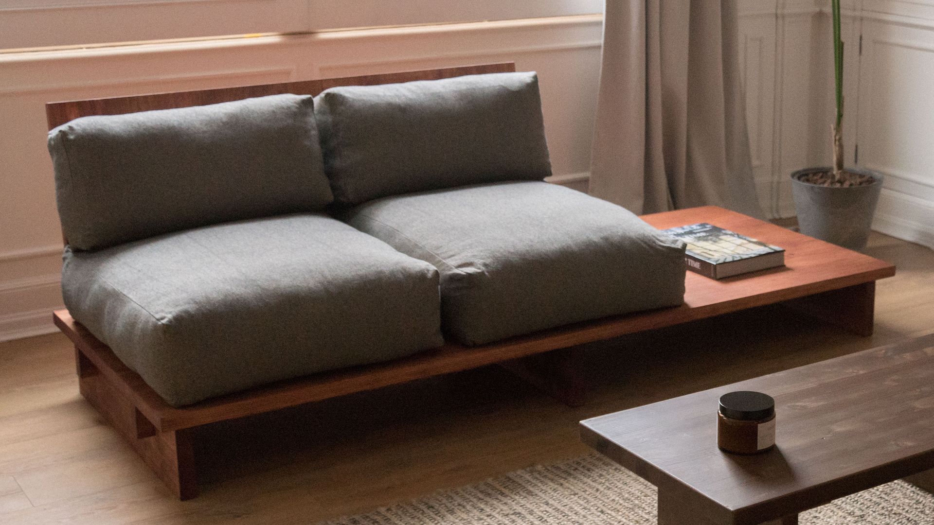 Salón con sofá con estructura de madera, asientos grises y mesa de madera integrada