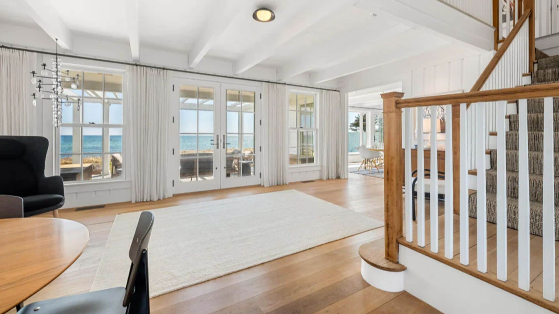 Casa taylor Swift recibidor con subida escalera con barandilla de madera, suelo de madera, ventanales con cortinas blancas, alfombra