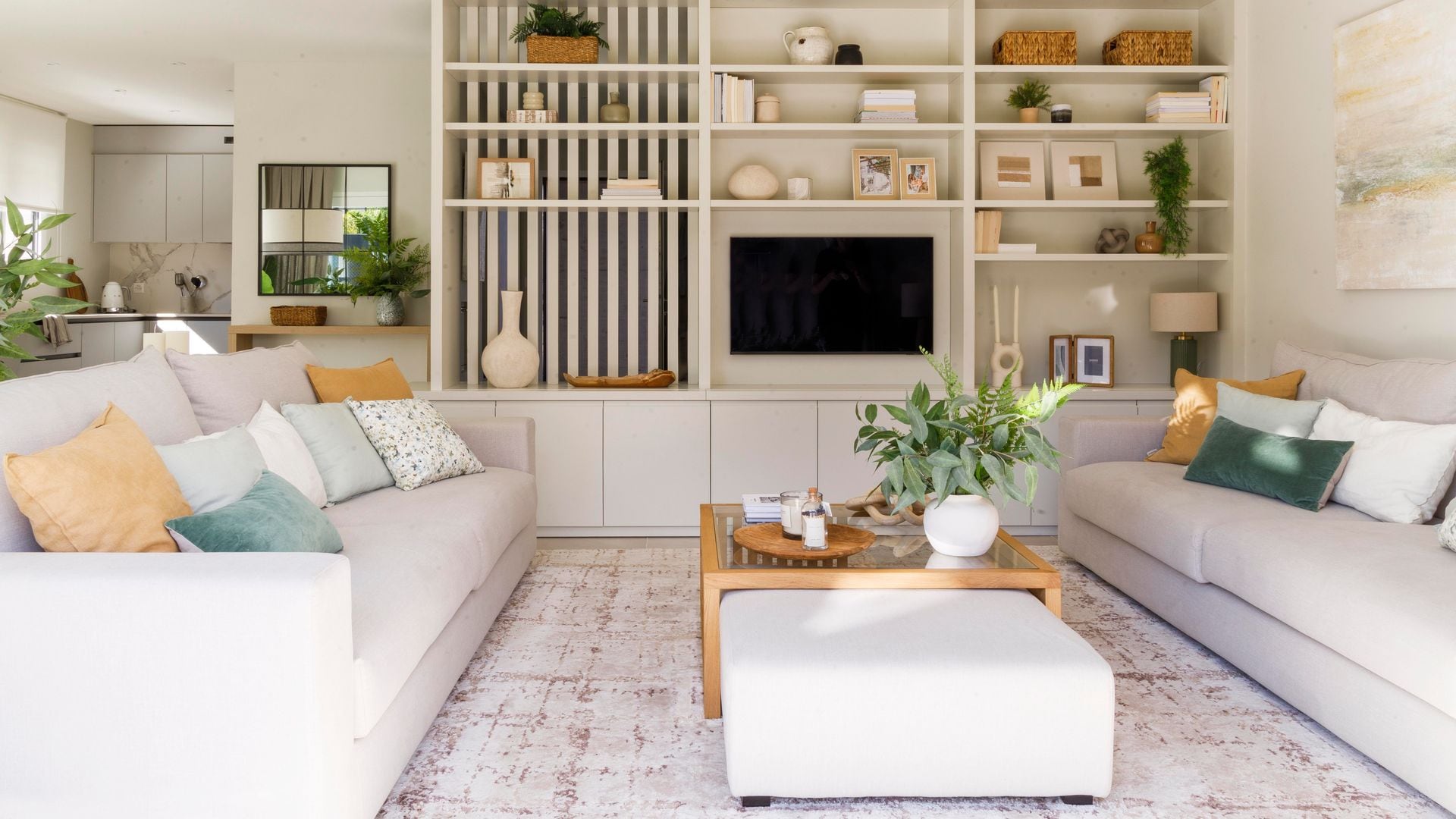 Salón con mueble a medida blanco, con hueco para la televisión, sofás blancos, mesa de centro de madera y tapizada, alfombra, cojines 