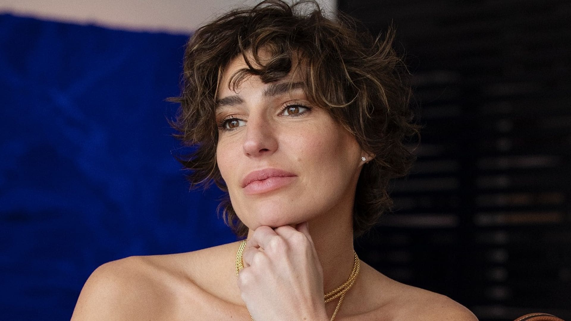 Eugenia Osborne sentada en una mesa con conjunto gris, bolso marrón y joyas doradas