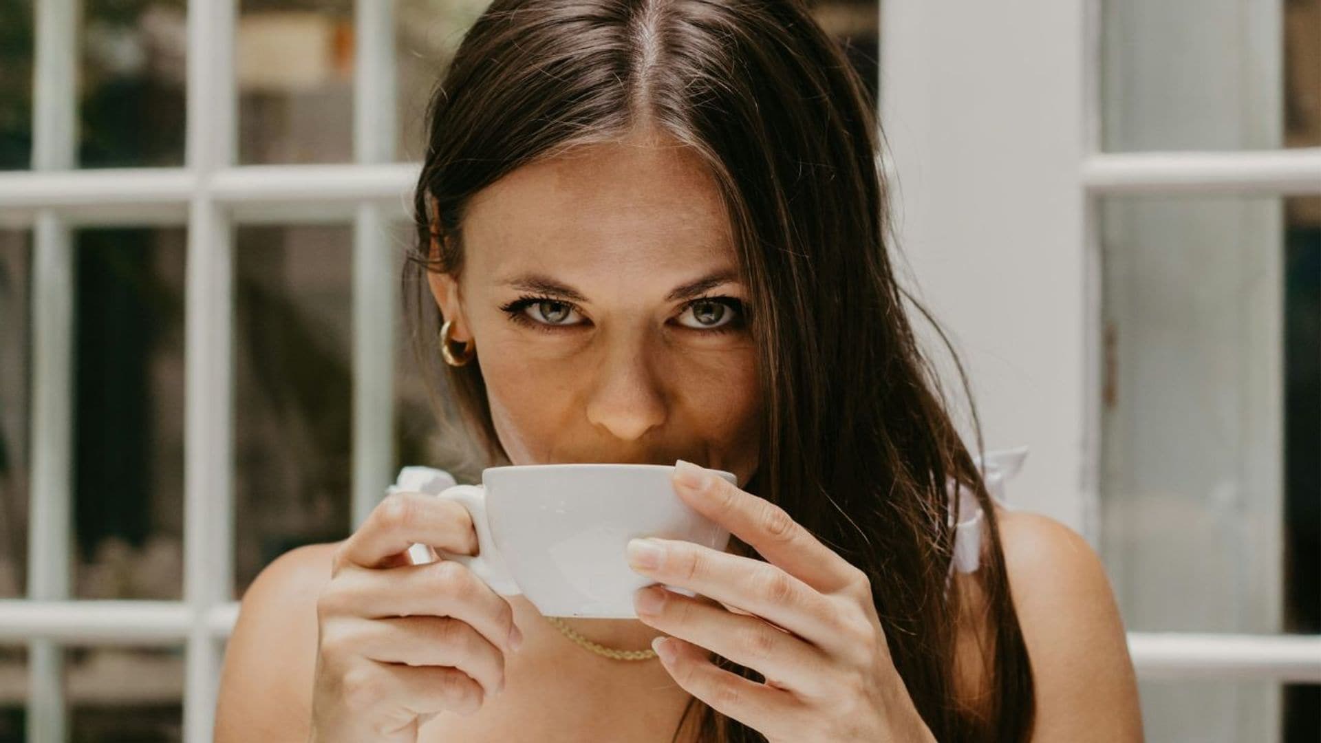 Mujer morena tomando café en una taza mirando a cámara