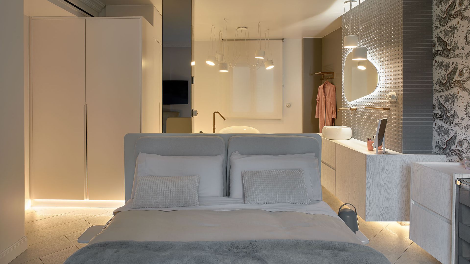 Dormitorio en suite en tonos grises, armario exento, lámparas y suelo iluminado 