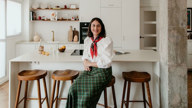 Retrato de la interiorista Anabel Soria en una cocina abierta blanca, con isla y taburetes de madera