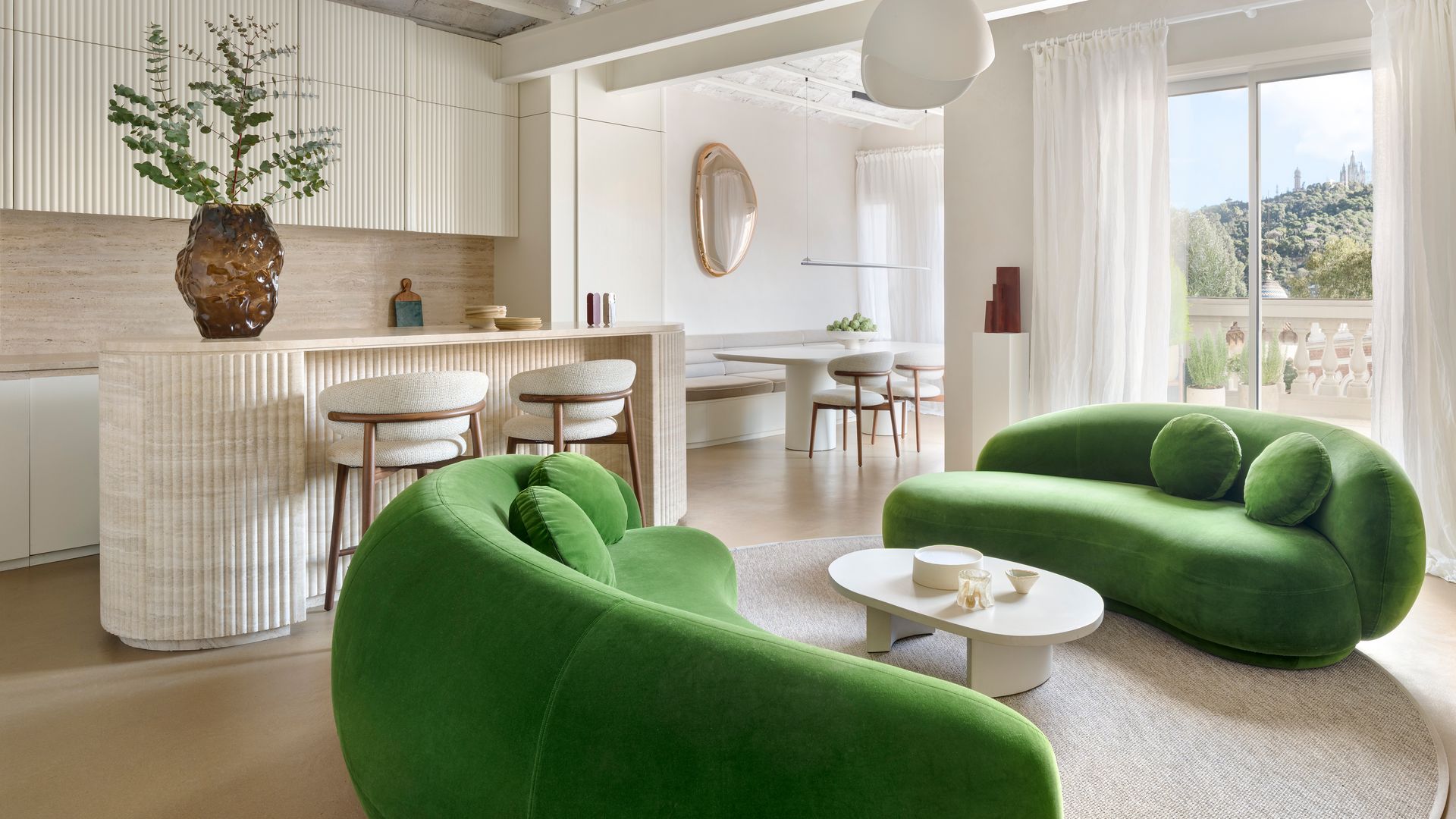 Salón, cocina con isla y comedor, sofás verdes, chimenea colgante, bóvedas catalanas, cortinas blancas