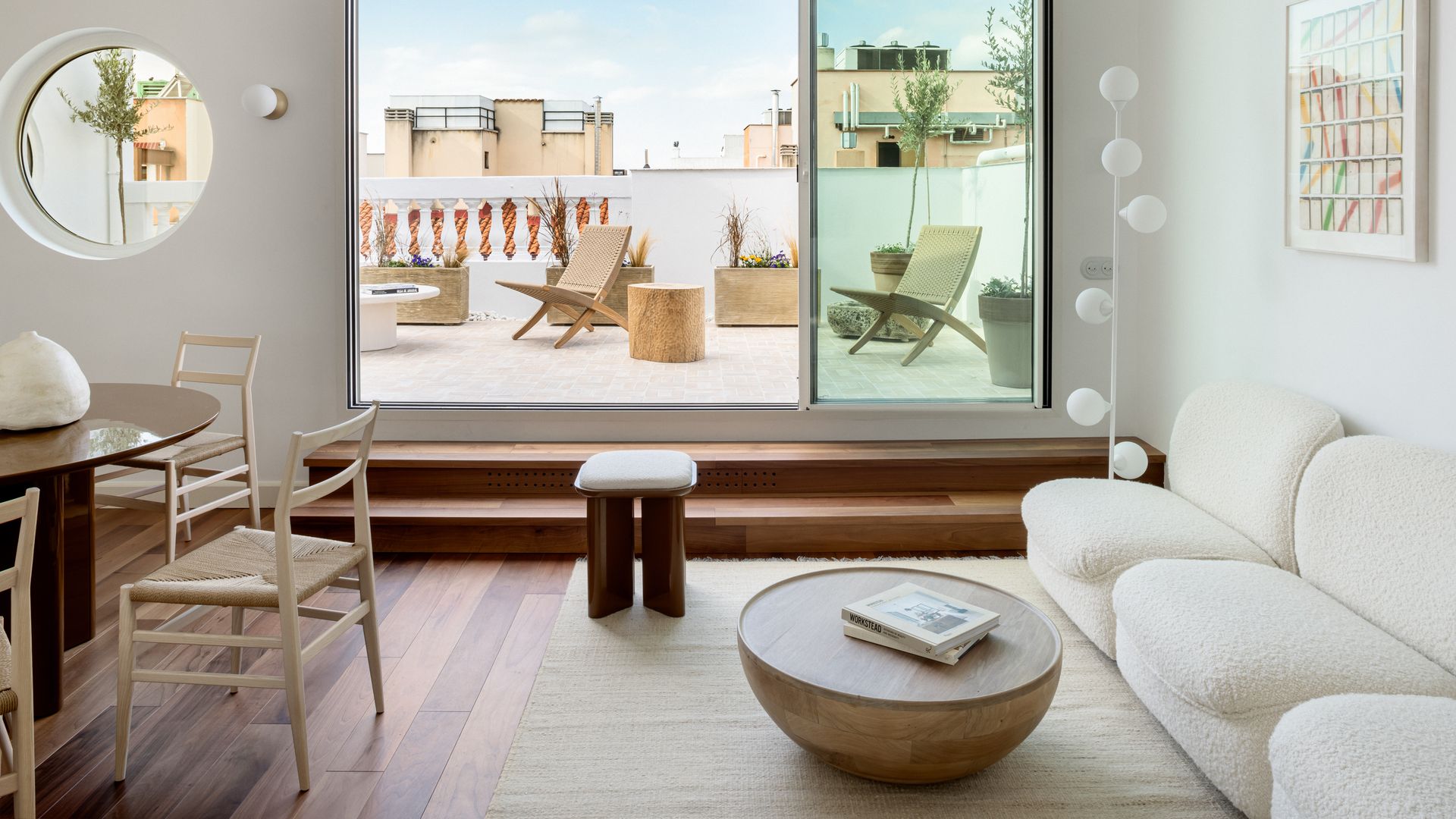 Salón comedor con sofá blanco y mesa de madera abierto a la terraza, con un gran ventanal corredero 