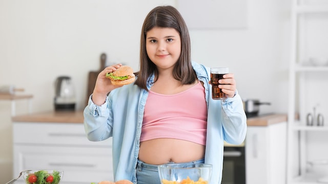 Niña con sobrepeso con comida basura en las manos