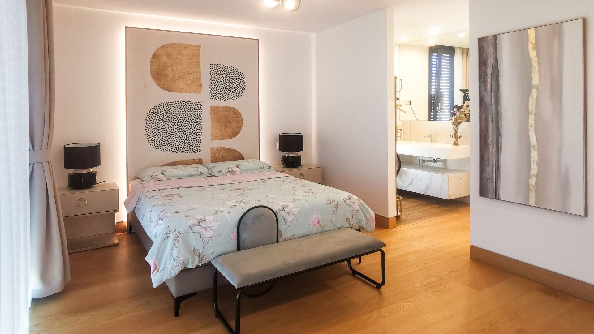 Cuarto de invitados con baño integrado, lámpara de techo, cuadros, suelo de madera y banqueta