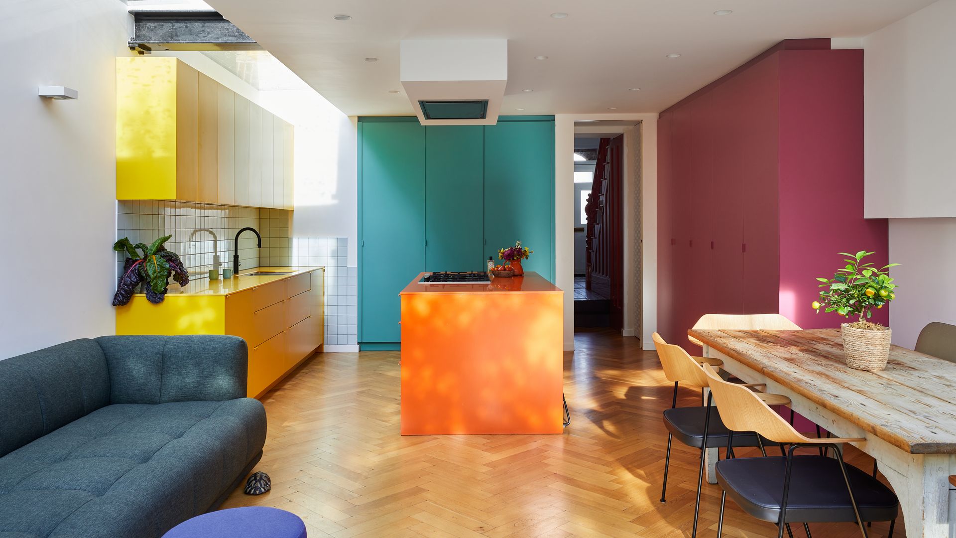 Cocina con isla, abierta al salón comedor, con muebles de color amarillo, naranja, burdeos y azul