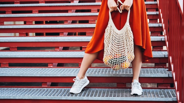 Mujer con zapatillas con una bolsa de red con naranjas en unas escaleras rojas