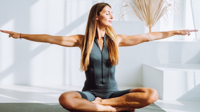 Mujer rubia practicando yoga en una sala blanca con esterilla
