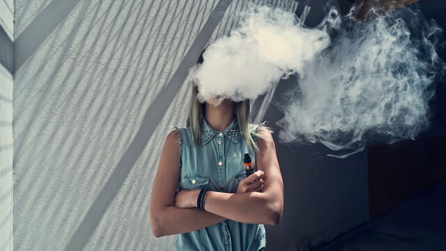 Chica adolescentes vapeando con una gran nube de humo sobre la cara
