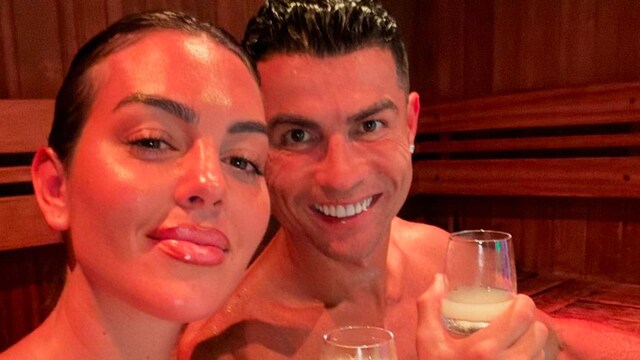 Plano medio de Georgina Rodríguez y Cristiano posando en un sauna rojo mientras toman una bebida