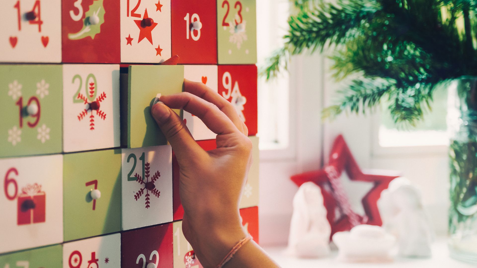 Mujer abriendo una de las casillas de un calendario de adviento en Navidad. Colores rojos, verdes y blancos.