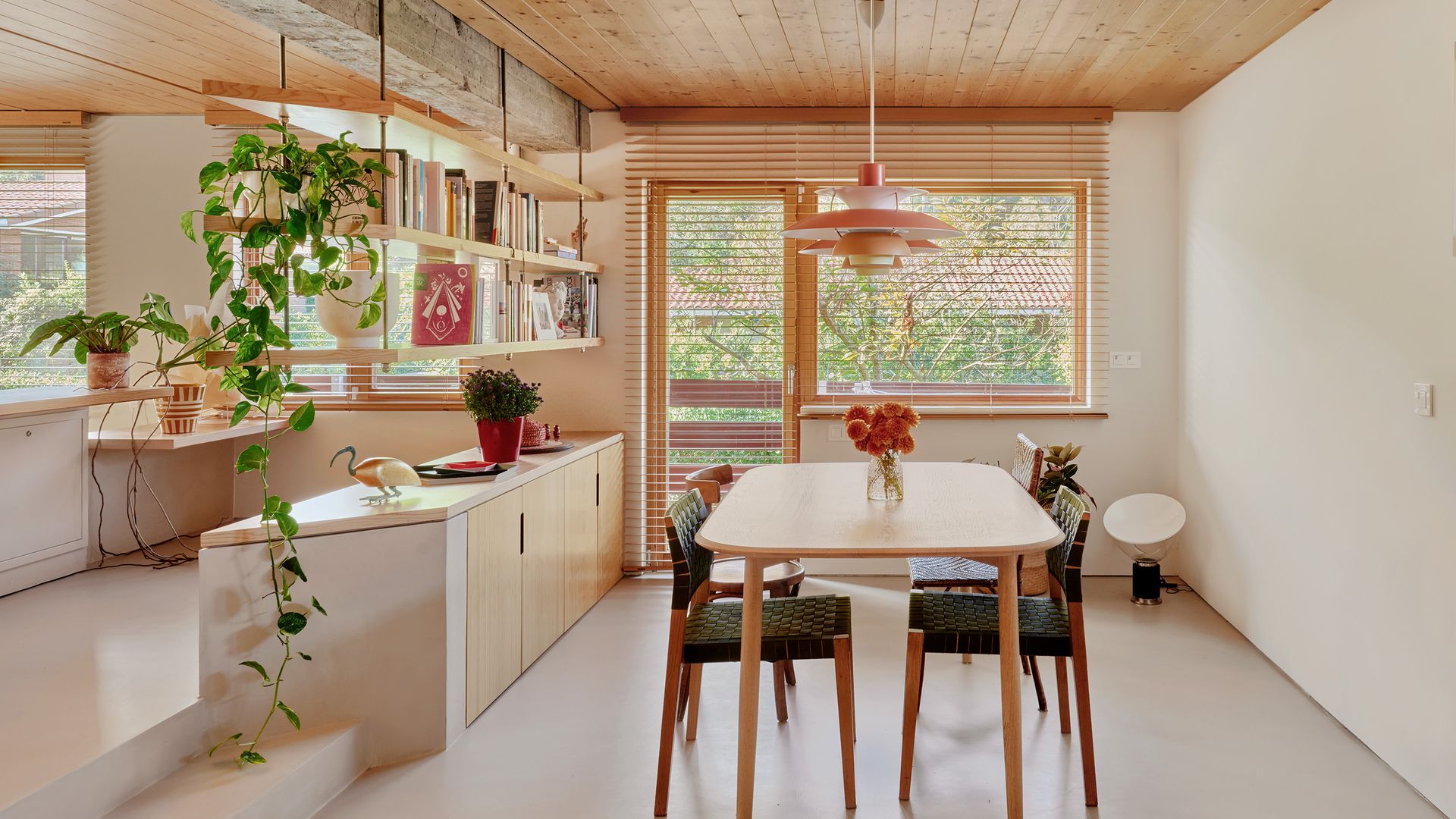 Comedor con mesa de madera, techo de madera, abierto a un despacho con estantería de madera flotante