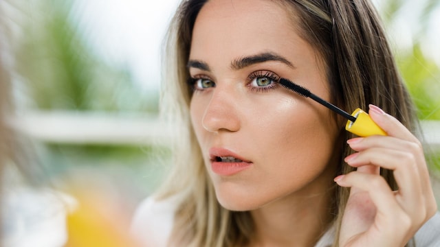 Rostro de mujer maquillándose con máscara de pestañas