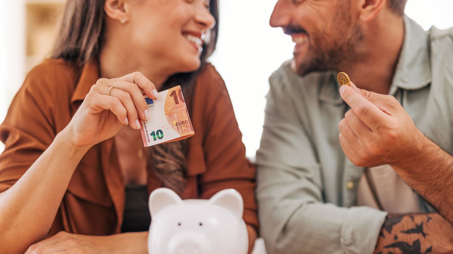 Pareja joven sonriente guardando dinero en una hucha para ahorrar e invertir en su futuro