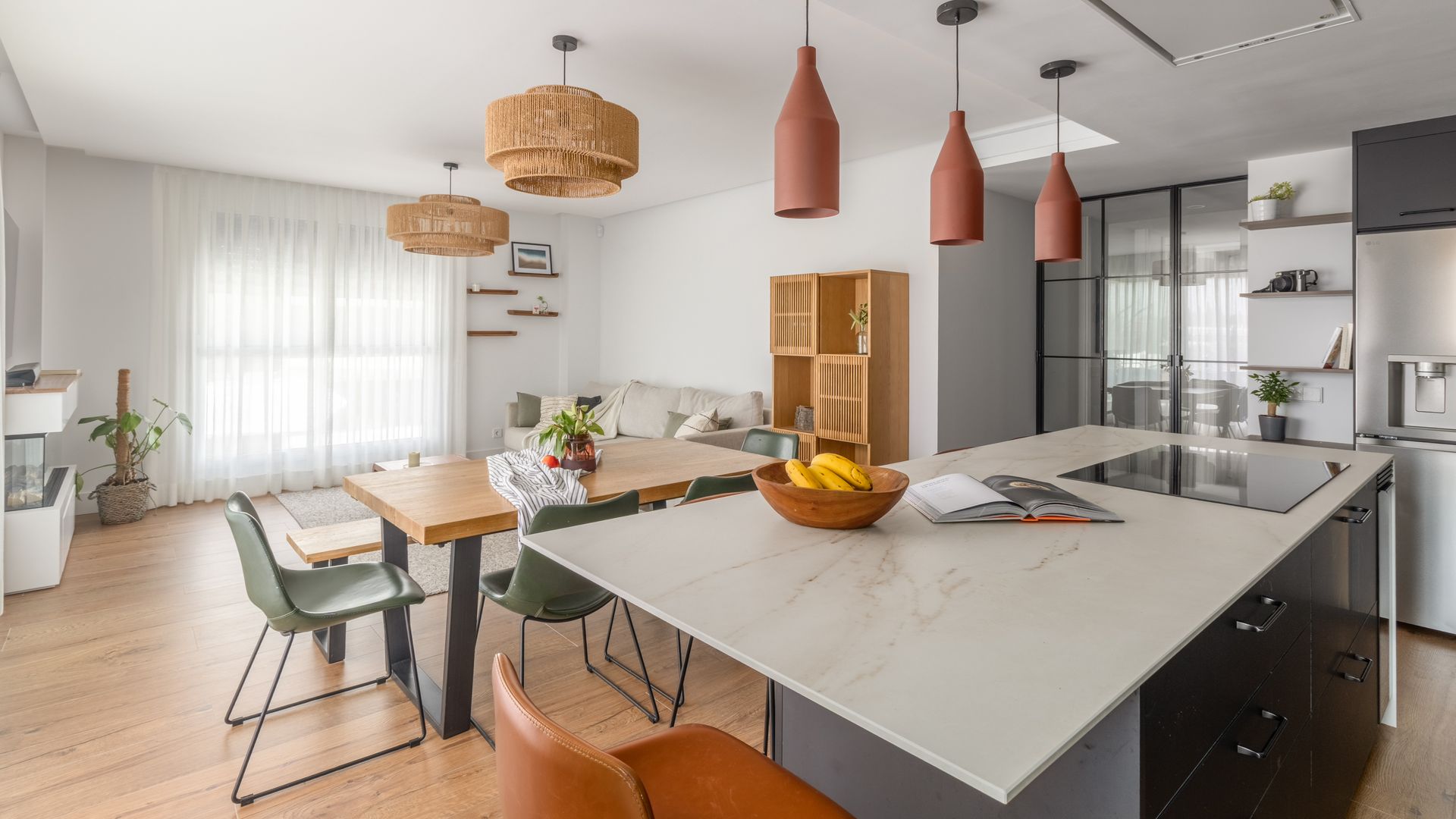Salón comedor cocina con isla, suelo de madera, cortinas blancas, lámparas de techo