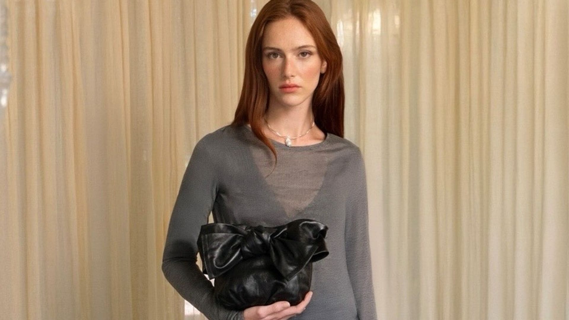 Mujer joven pelirroja con falda de lentejuelas, jersey de punto y bolso con lazo de malababa