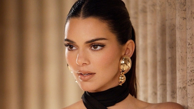 Kendall Jenner con vestido negro asimétrico, cabello recogido en una coleta y pendientes dorados