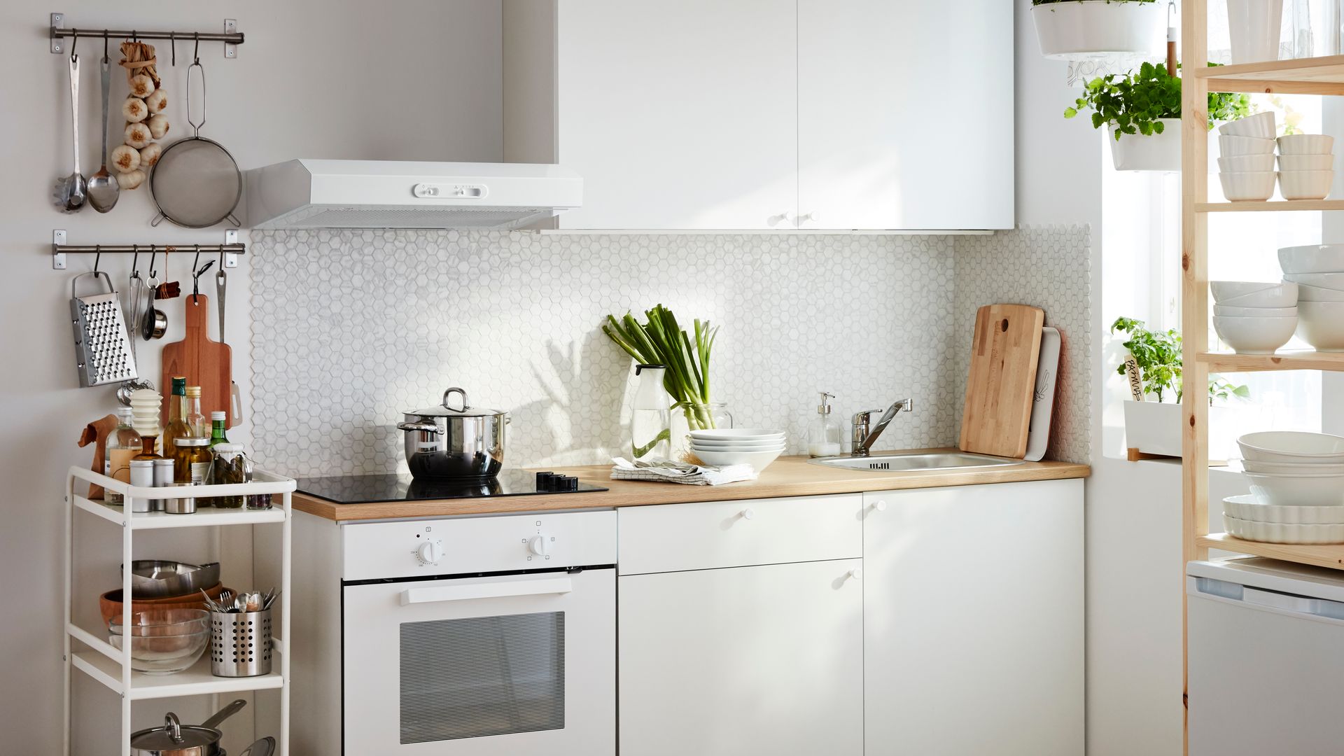 Cocina IKEA con muebles blancos, carrito, plantas, alfombra de fibras naturales