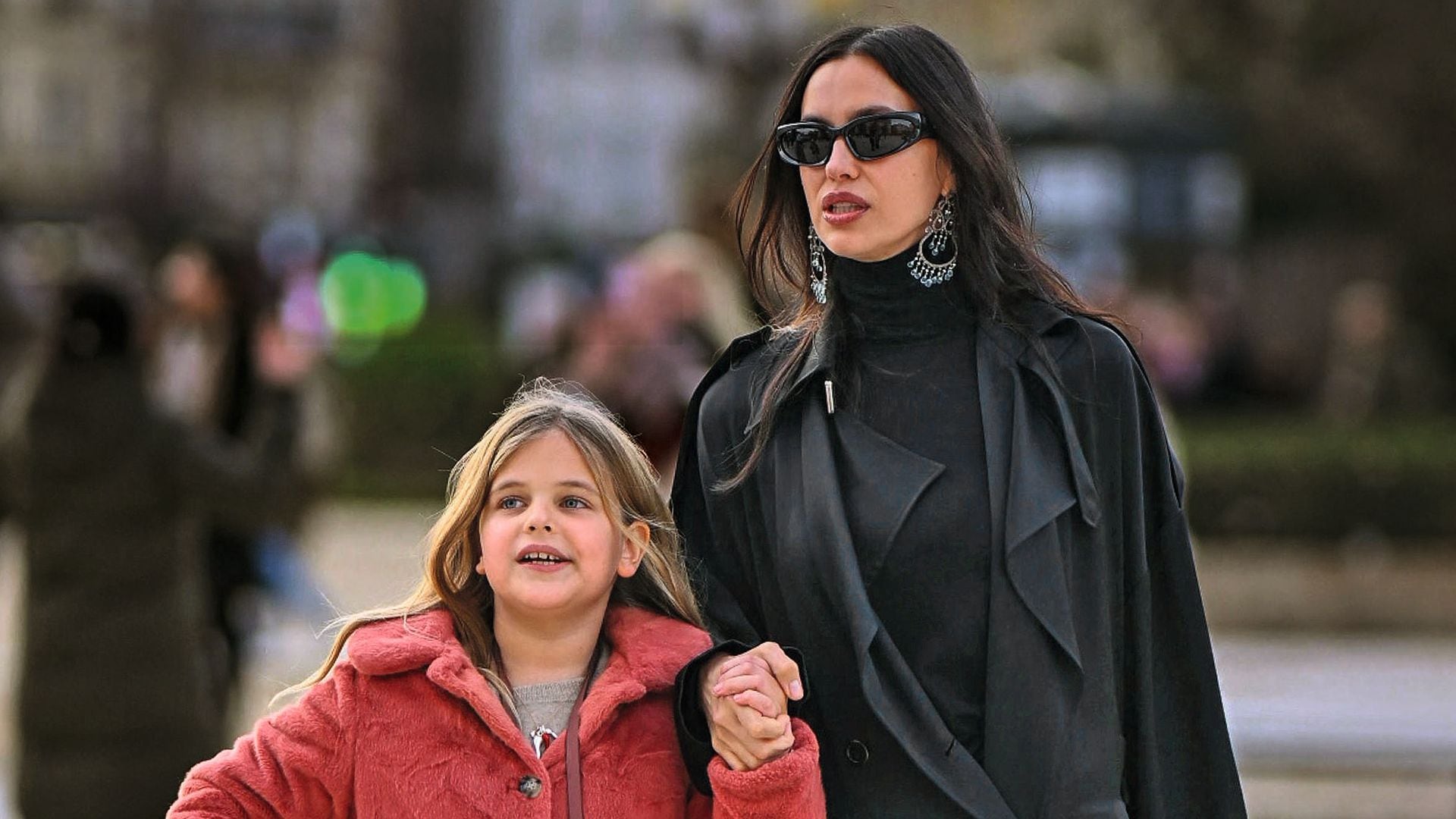 Irina Shayk, con gafas de sol y abrigo negro, camina con una niña en abrigo rojo.