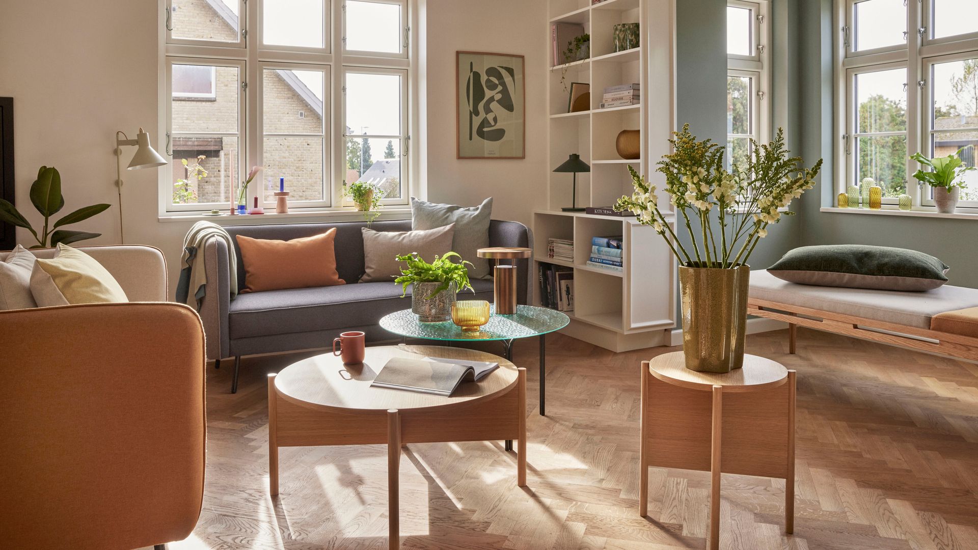 Salón con sofá gris, grandes ventanales, rincón con daybed, mesas de centro de madera, mesa auxiliar de cristal, estantería 