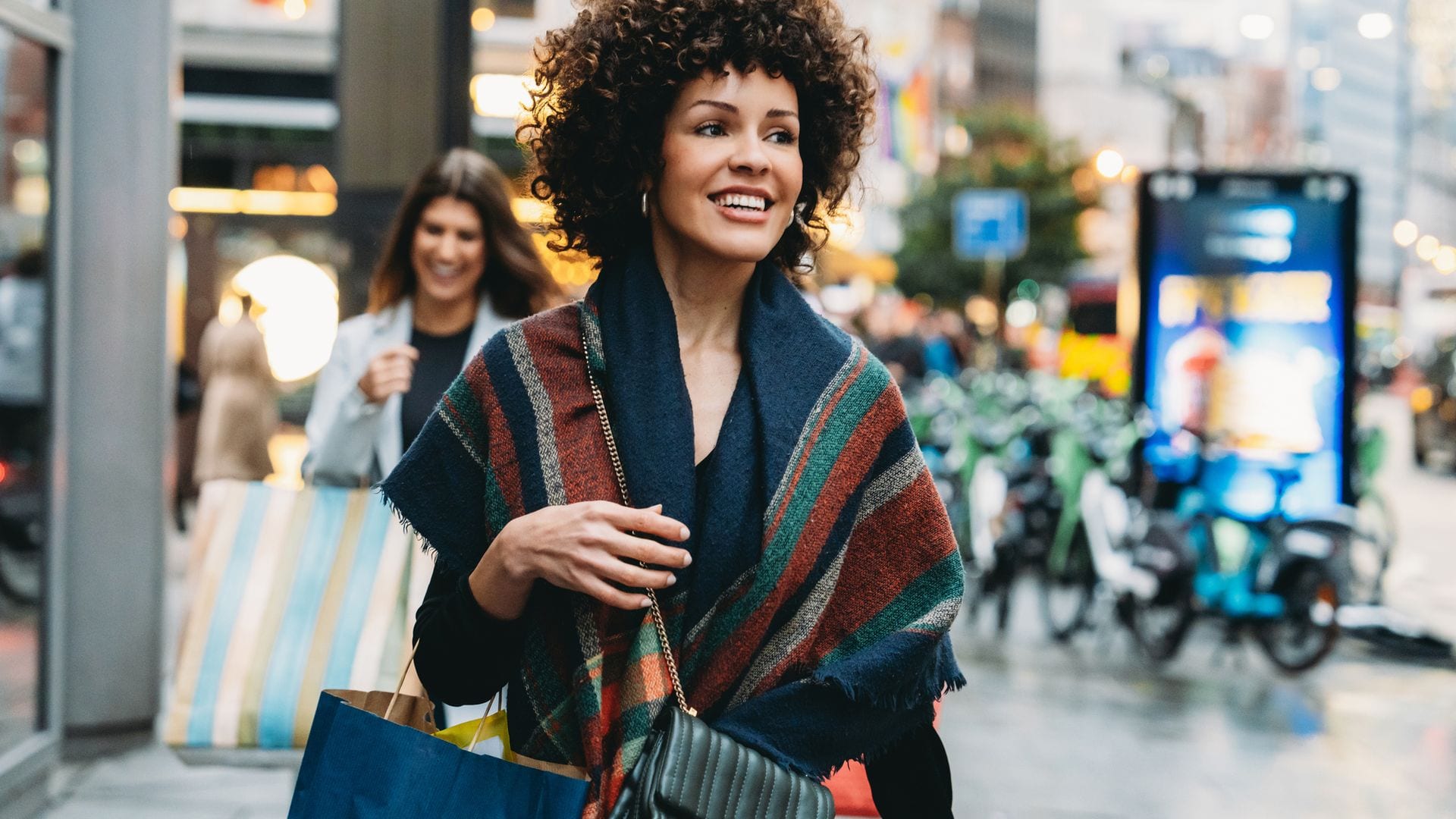 Mujer llevando bolsas de la compra en la calle, en primer plano, después de haber llovido con ropa otoño-invierno.