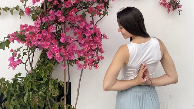 Mujer joven haciendo una postura de yoga junto a una buganvilla