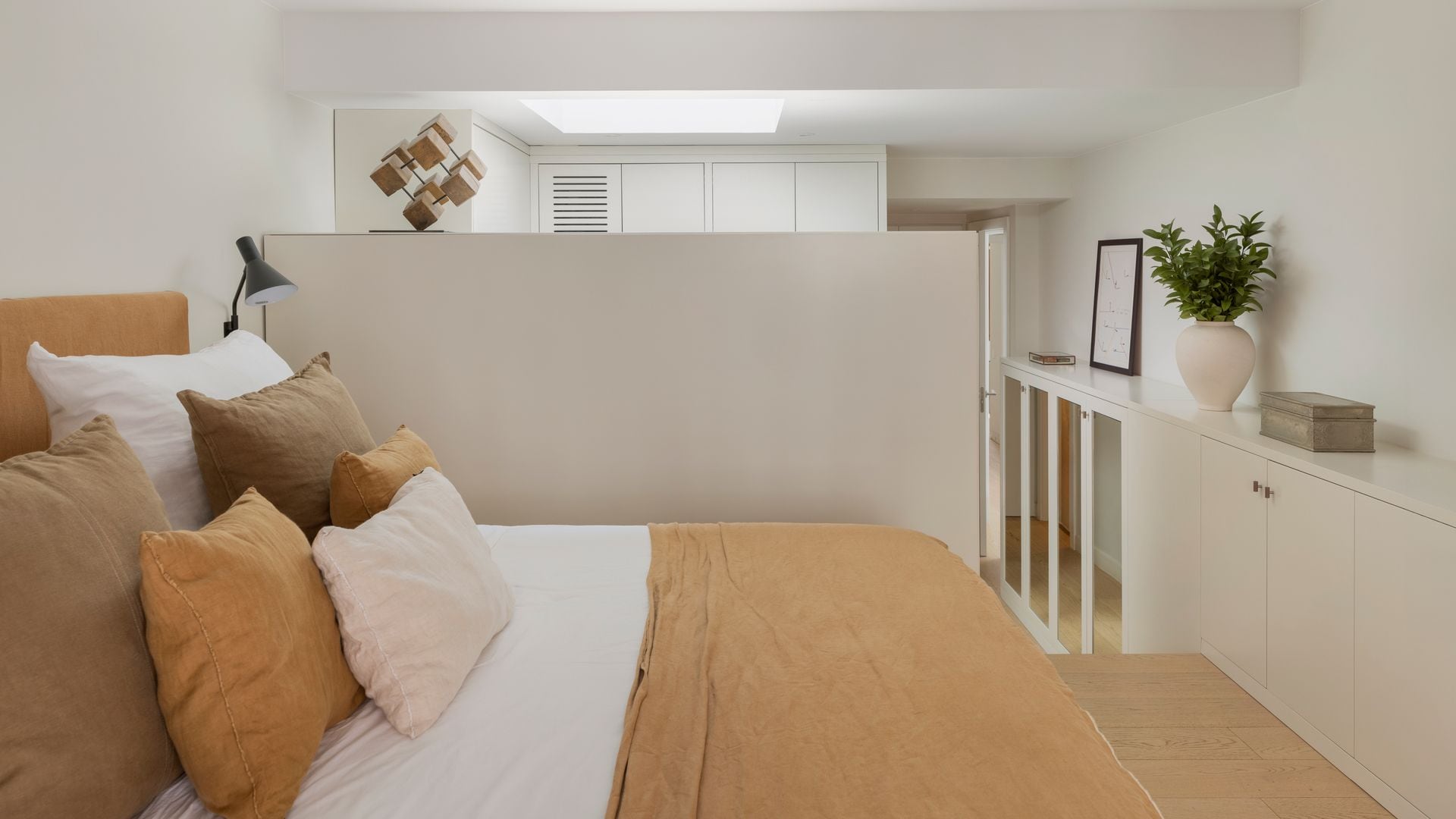 Dormitorio con ropa de cama beige y mueble bajo a medida con puertas y vitrinas
