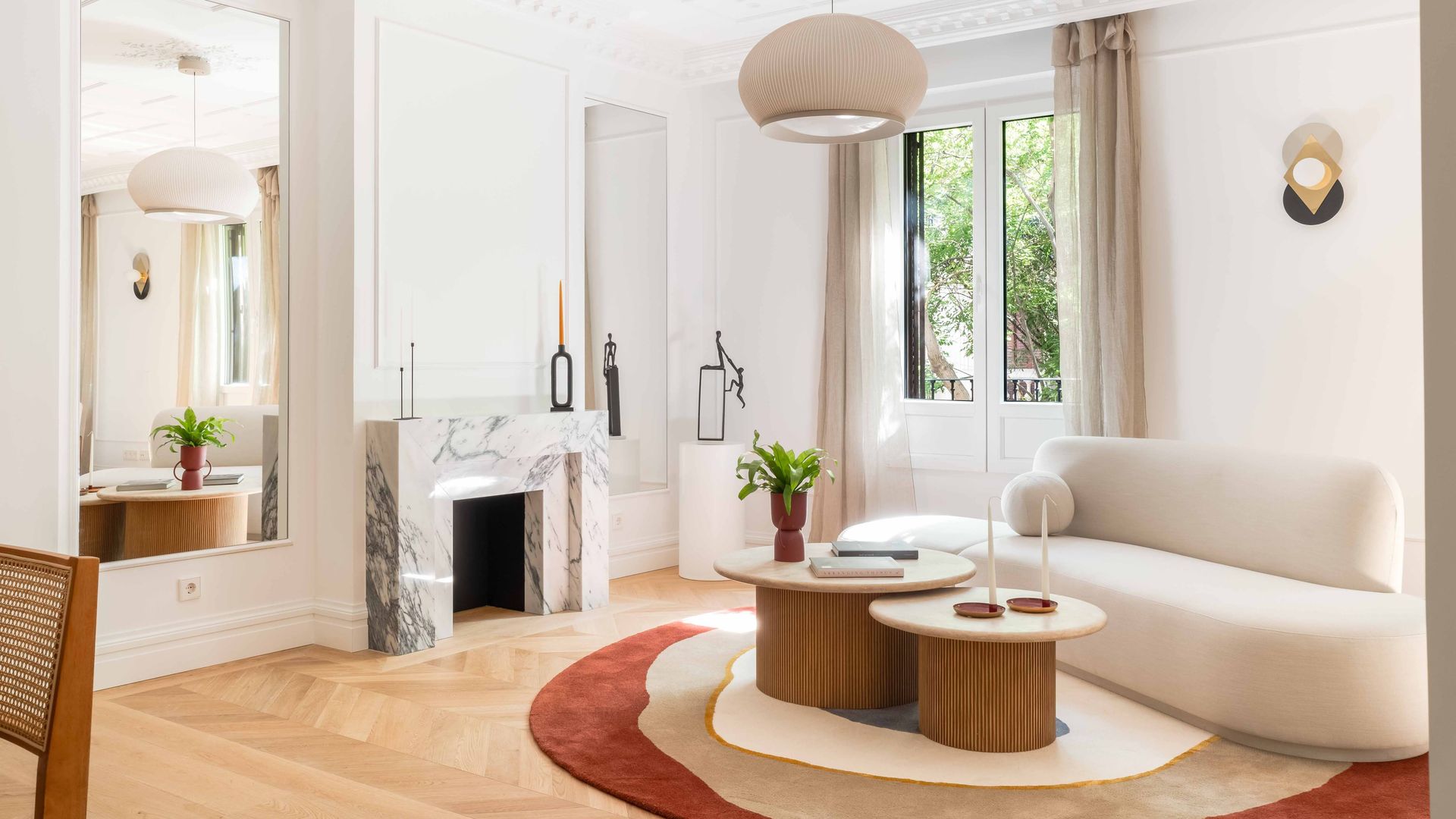 Salón con chimenea, sofá blanco de formas curvas, alfombras, mesas hechas a mano de madera, espejo, molduras en el techo