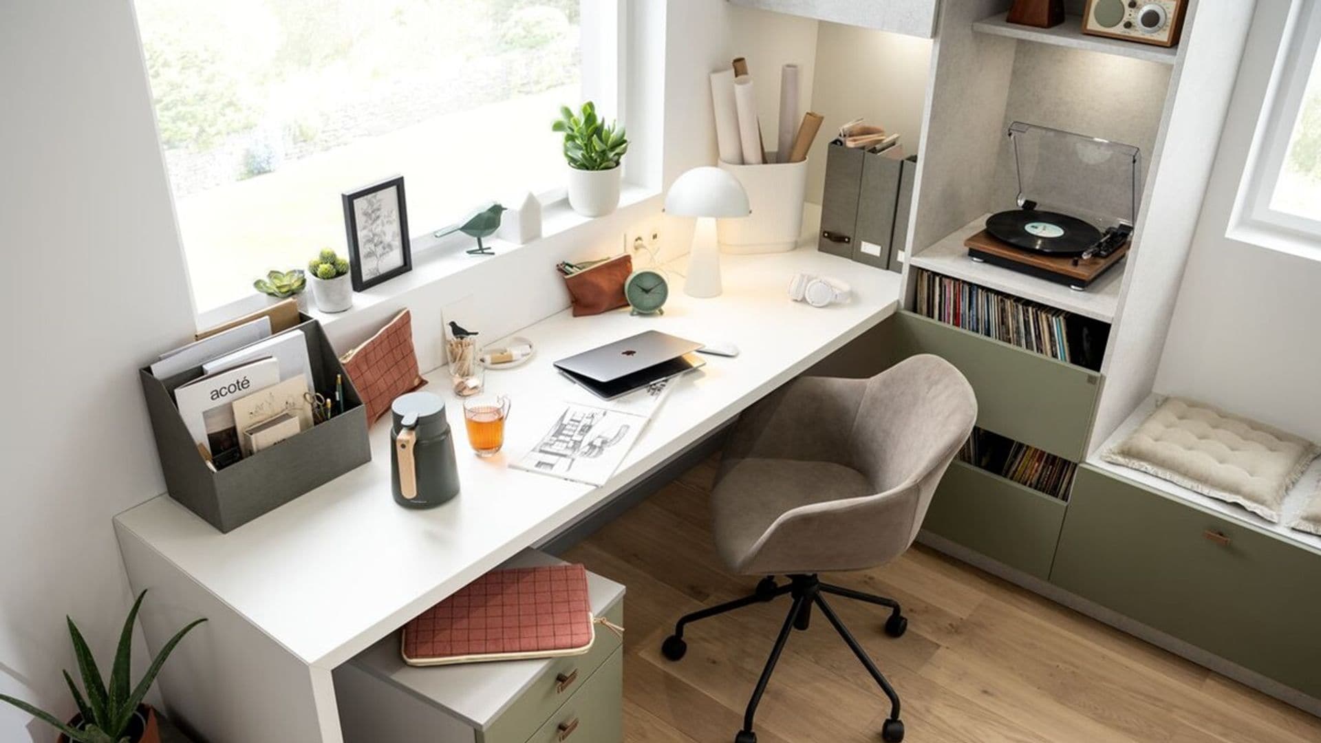 Zona de escritorio con mesa blanca, cajonera, banco con cojines, estantería, ventana y estores blancos