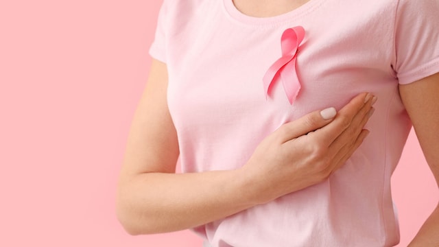 mujer palpándose el pecho, con una camiseta rosa con un lazo